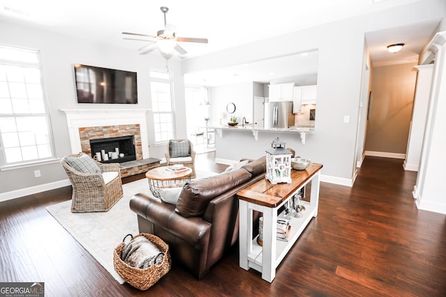 living room featuring a fireplace, a ceiling fan, visible vents, baseboards, and dark wood-style floors