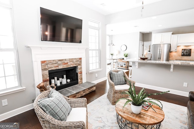 living room with dark wood-style floors, a stone fireplace, and baseboards