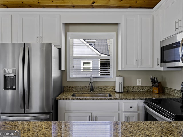 kitchen with white cabinetry, appliances with stainless steel finishes, dark stone counters, and a sink