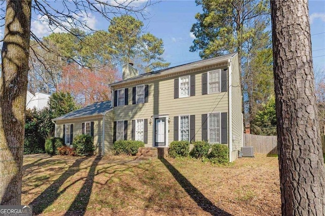 colonial house with a chimney, fence, cooling unit, and a front yard