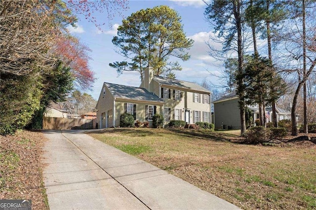 view of front of home featuring an attached garage, concrete driveway, a chimney, and a front yard