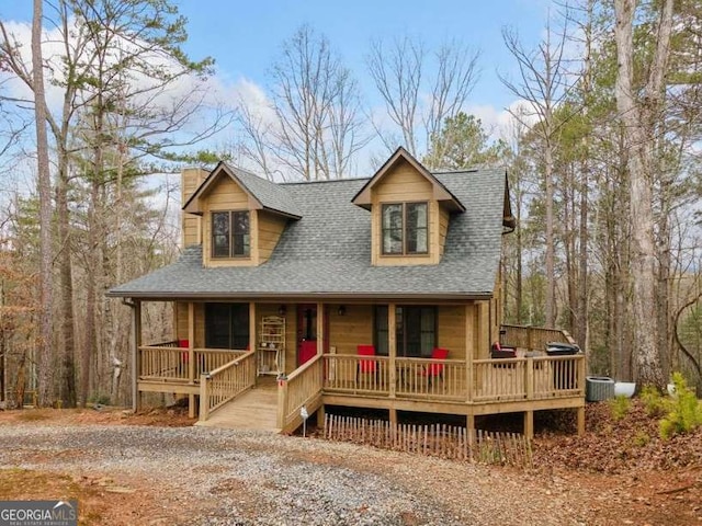 chalet / cabin featuring covered porch, a shingled roof, a chimney, and central AC