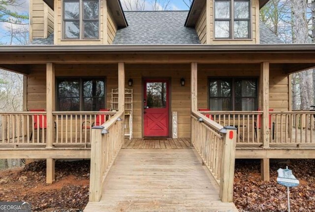 entrance to property with covered porch and roof with shingles