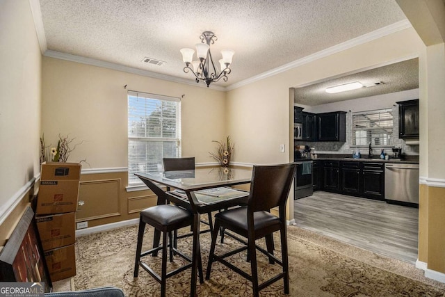 dining area with a textured ceiling, a wainscoted wall, visible vents, ornamental molding, and an inviting chandelier