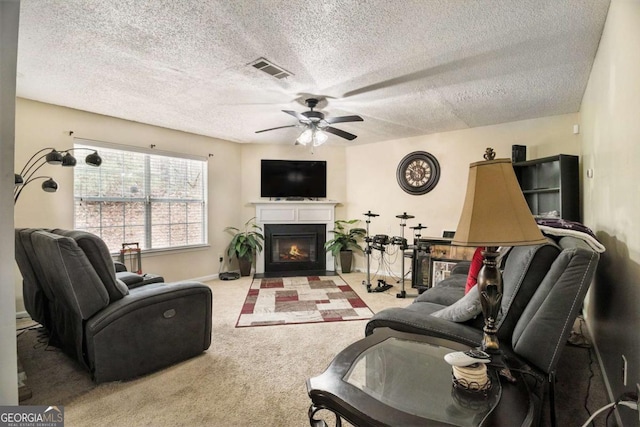 carpeted living room featuring baseboards, visible vents, a ceiling fan, a glass covered fireplace, and a textured ceiling