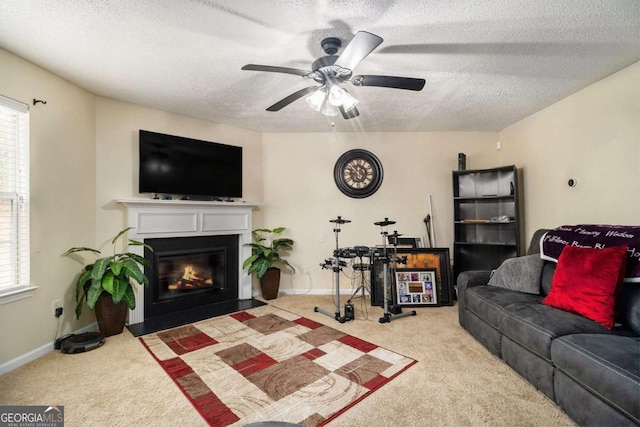 living area featuring baseboards, a ceiling fan, a fireplace with flush hearth, a textured ceiling, and carpet floors