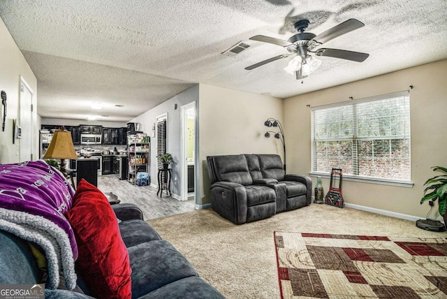 living area with visible vents, light carpet, ceiling fan, a textured ceiling, and baseboards