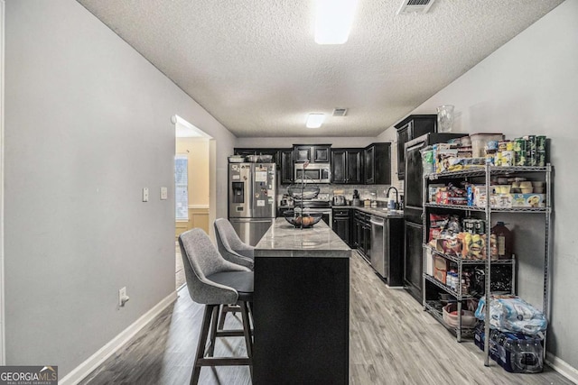 kitchen with a center island, stainless steel appliances, light wood-style flooring, a sink, and dark cabinets