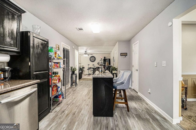 kitchen with light wood finished floors, visible vents, a ceiling fan, dark cabinets, and a textured ceiling