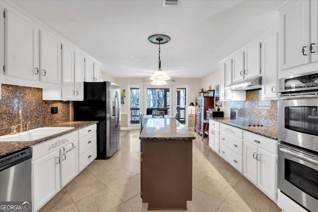 kitchen with under cabinet range hood, stainless steel appliances, a sink, white cabinetry, and a center island