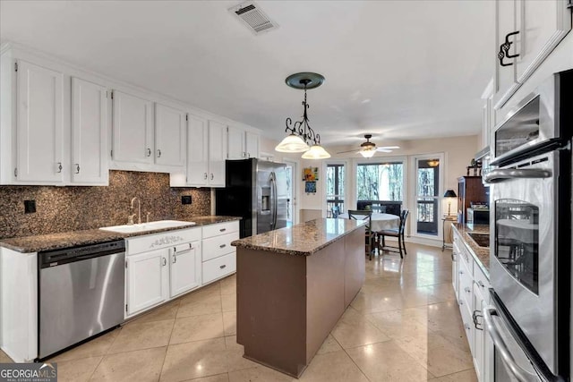 kitchen featuring visible vents, backsplash, appliances with stainless steel finishes, a sink, and a kitchen island