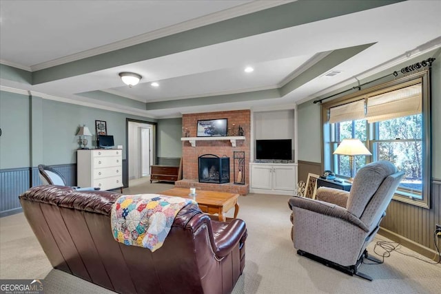 carpeted living room with a tray ceiling, crown molding, visible vents, a brick fireplace, and wainscoting