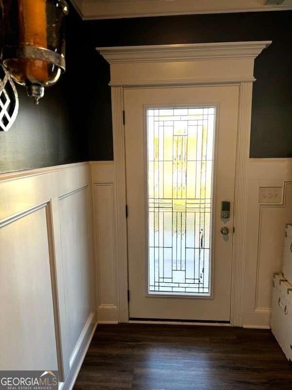 doorway to outside with a wainscoted wall, dark wood-style flooring, and a decorative wall