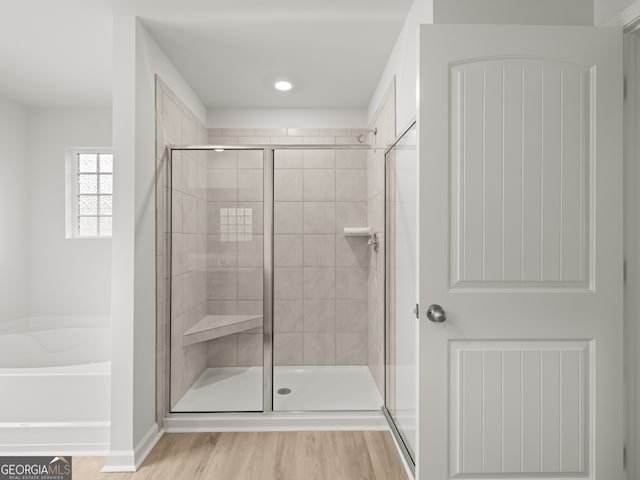 full bath featuring a stall shower, a garden tub, and wood finished floors