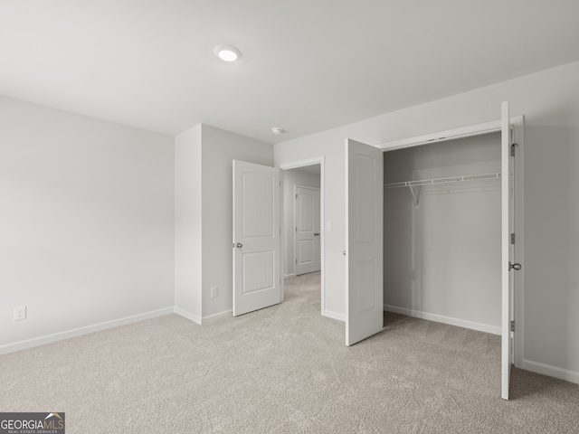 unfurnished bedroom with baseboards, a closet, and light colored carpet