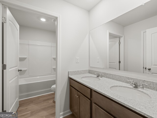 bathroom featuring double vanity, wood finished floors, a sink, and toilet