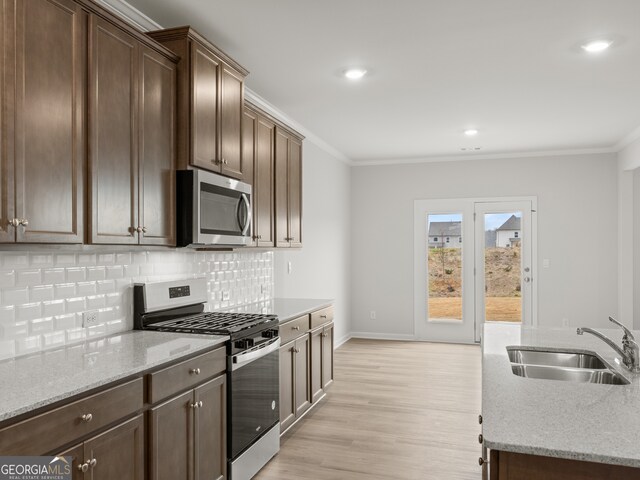 kitchen featuring a sink, ornamental molding, appliances with stainless steel finishes, backsplash, and light wood finished floors