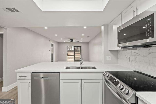 kitchen with a peninsula, a sink, visible vents, white cabinets, and appliances with stainless steel finishes