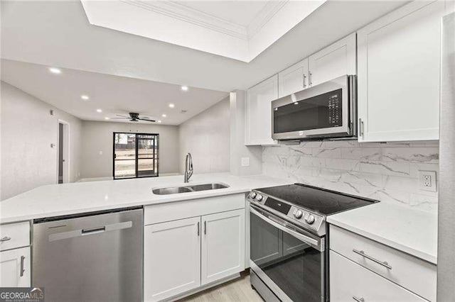 kitchen featuring a peninsula, a sink, white cabinetry, light countertops, and appliances with stainless steel finishes