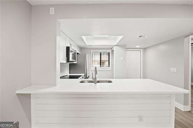 kitchen featuring stainless steel microwave, a peninsula, light countertops, white cabinetry, and a sink