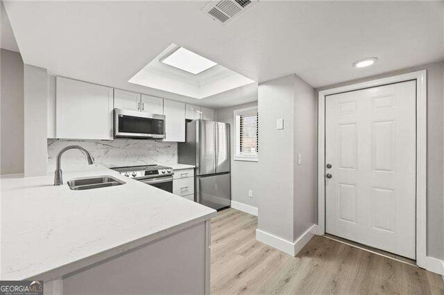 kitchen featuring tasteful backsplash, light wood-style flooring, appliances with stainless steel finishes, white cabinetry, and a sink