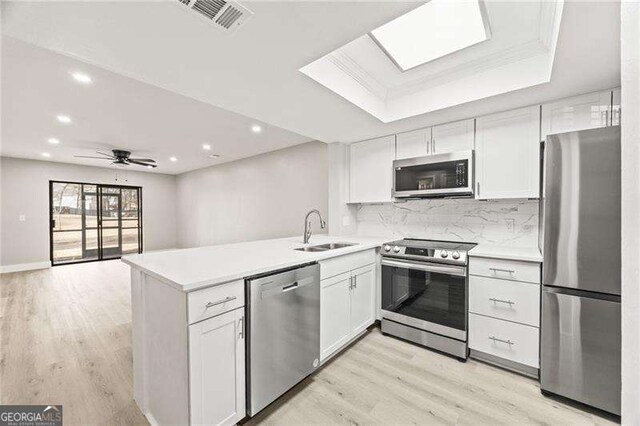 kitchen featuring visible vents, a raised ceiling, appliances with stainless steel finishes, a peninsula, and a sink