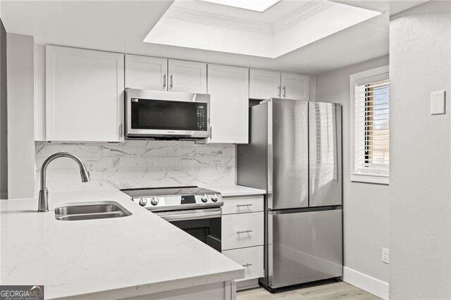 kitchen with stainless steel appliances, white cabinetry, a sink, and backsplash