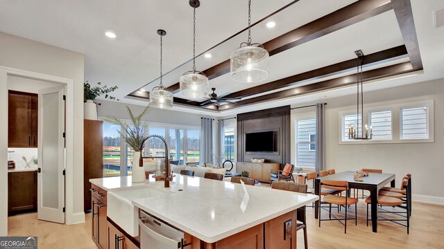 kitchen with light wood-type flooring, a tray ceiling, dishwasher, and a sink