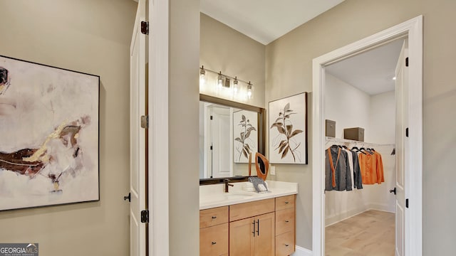 bathroom featuring wood finished floors, a walk in closet, vanity, and baseboards