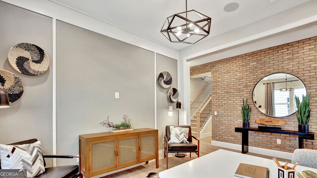 sitting room with a notable chandelier, brick wall, baseboards, stairs, and light wood finished floors