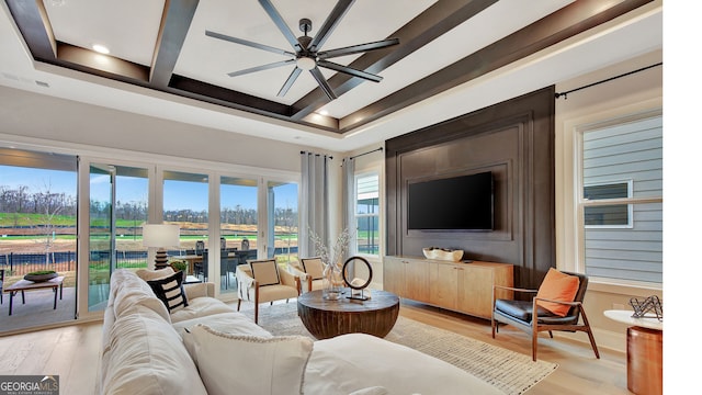 living area featuring coffered ceiling, a ceiling fan, baseboards, light wood-type flooring, and beam ceiling