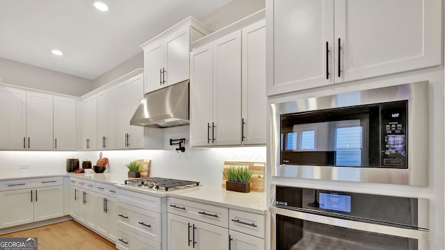 kitchen with stainless steel appliances, tasteful backsplash, white cabinets, and under cabinet range hood