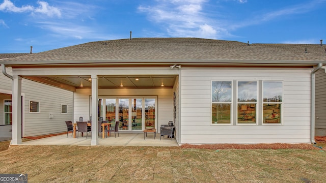 back of property featuring a shingled roof, a patio, and a lawn