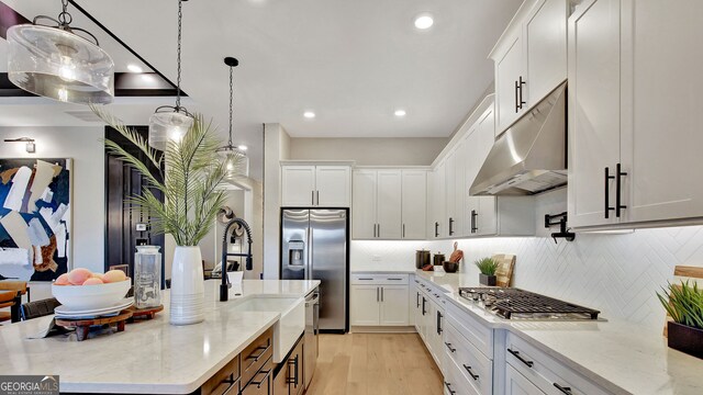 kitchen with decorative backsplash, appliances with stainless steel finishes, white cabinets, light wood-type flooring, and under cabinet range hood