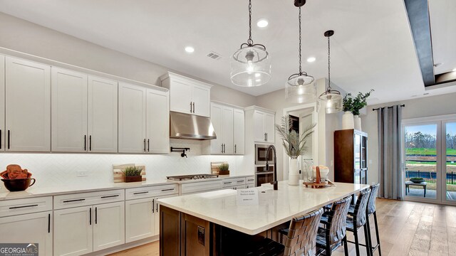 kitchen with visible vents, white cabinets, decorative backsplash, light wood-style flooring, and under cabinet range hood