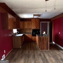 kitchen with brown cabinetry, dark countertops, dark wood finished floors, and baseboards