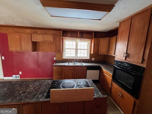 kitchen featuring visible vents, brown cabinetry, white dishwasher, a sink, and black oven