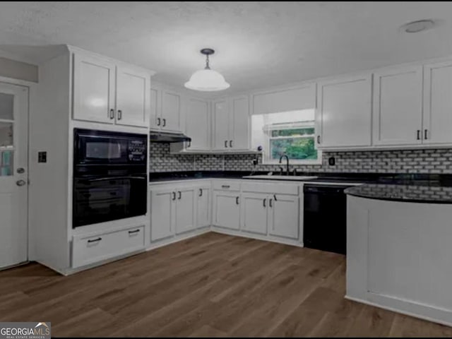 kitchen featuring dark countertops, white cabinetry, a sink, under cabinet range hood, and black appliances