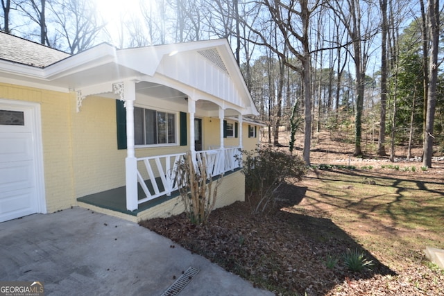 view of side of home with a garage, brick siding, a porch, and roof with shingles