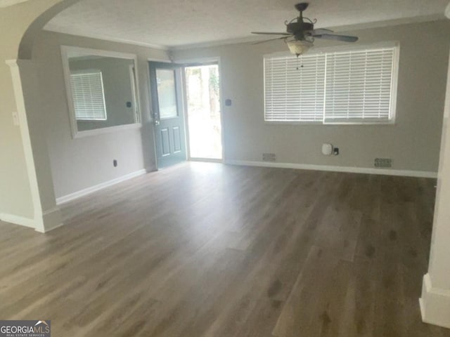 unfurnished living room featuring arched walkways, baseboards, and wood finished floors