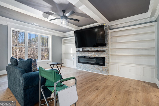 living room featuring crown molding, built in features, a stone fireplace, wood finished floors, and a ceiling fan