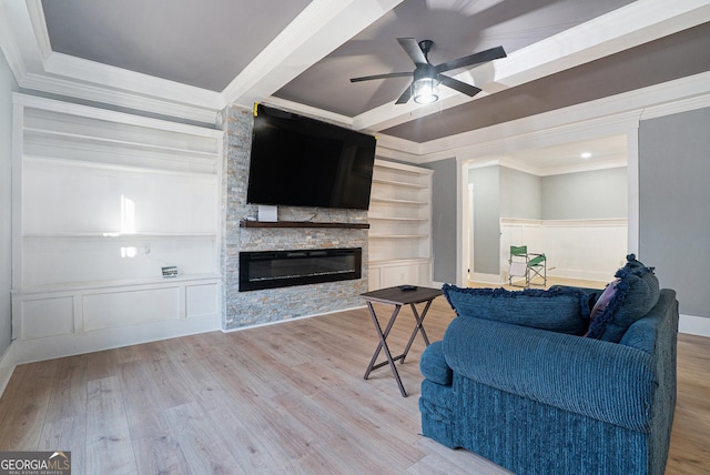 living room with built in shelves, wood finished floors, a stone fireplace, crown molding, and ceiling fan