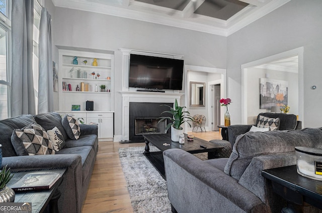 living room with light wood finished floors, a fireplace with raised hearth, beamed ceiling, ornamental molding, and coffered ceiling