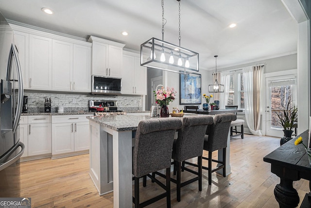 kitchen with light wood finished floors, backsplash, light stone countertops, stainless steel appliances, and white cabinetry