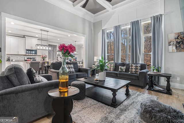 living room featuring beamed ceiling, ornamental molding, coffered ceiling, light wood finished floors, and ceiling fan