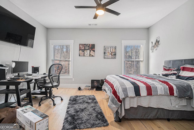 bedroom with a ceiling fan, wood finished floors, visible vents, and baseboards