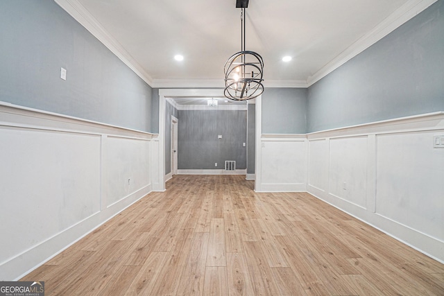 unfurnished dining area with wood finished floors, a wainscoted wall, visible vents, ornamental molding, and a notable chandelier