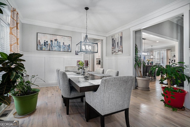 dining space with hardwood / wood-style floors, a wainscoted wall, crown molding, a decorative wall, and a notable chandelier