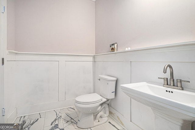 bathroom with a sink, a wainscoted wall, toilet, and marble finish floor