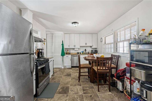 kitchen with white cabinets, stone finish flooring, ventilation hood, stainless steel appliances, and backsplash